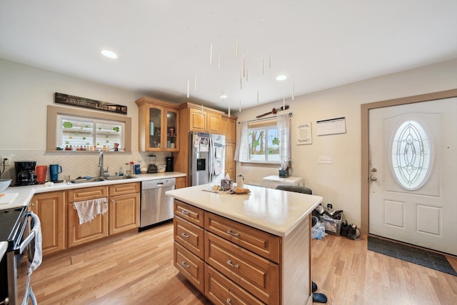 kitchen with light wood-style floors, decorative backsplash, a sink, and stainless steel appliances