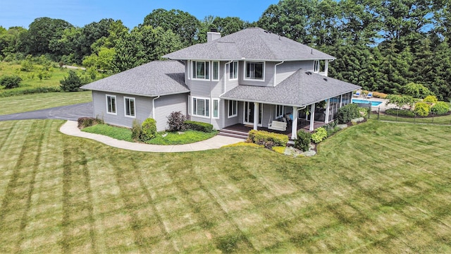view of front facade featuring a chimney, an outdoor pool, a front lawn, a shingled roof, and covered porch