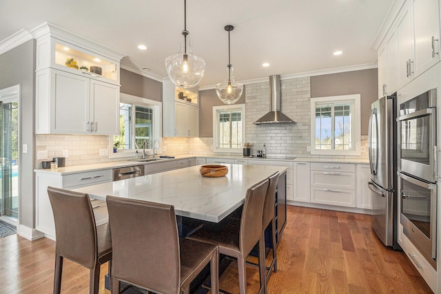kitchen with wall chimney exhaust hood, appliances with stainless steel finishes, a breakfast bar, white cabinetry, and wood finished floors