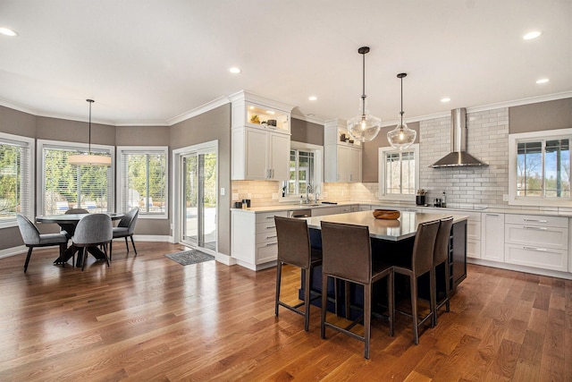 kitchen featuring a center island, white cabinets, dark wood-style flooring, wall chimney range hood, and light countertops