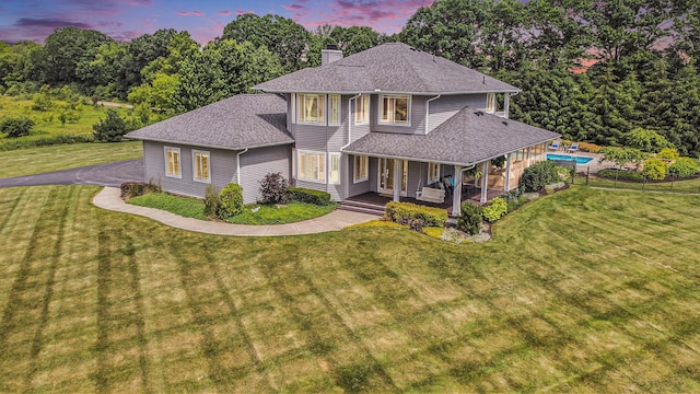 view of front facade featuring a front yard, covered porch, a chimney, an outdoor pool, and roof with shingles