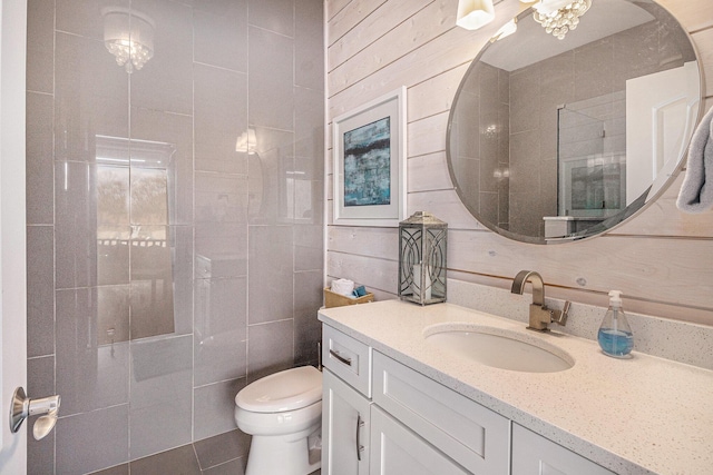 bathroom featuring tiled shower, vanity, tile patterned flooring, toilet, and tile walls