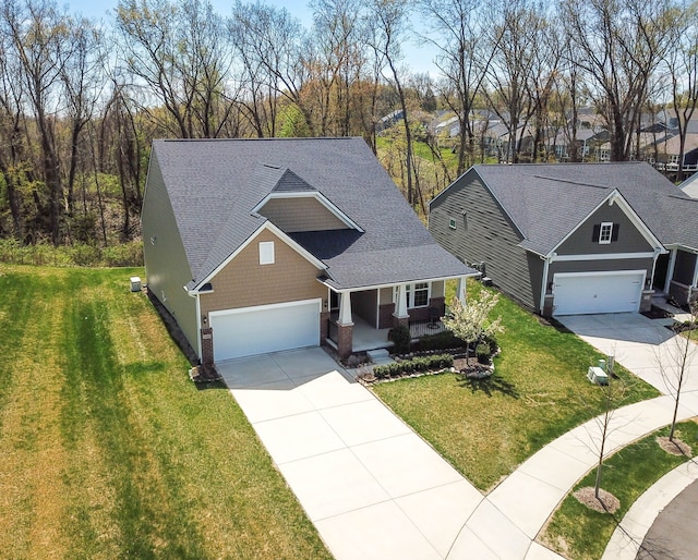 view of front facade with driveway, roof with shingles, covered porch, and a front yard