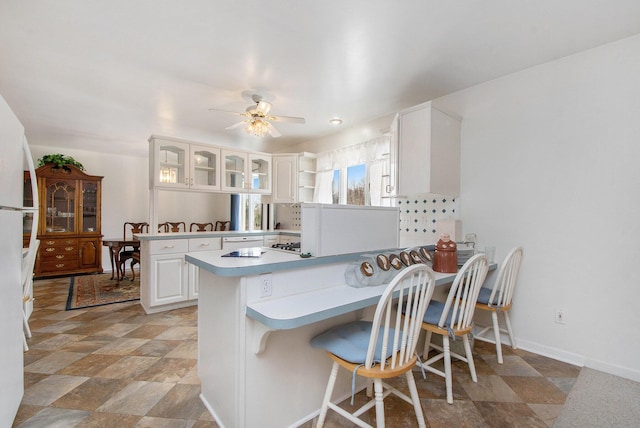 kitchen with white cabinets, a ceiling fan, a peninsula, and baseboards