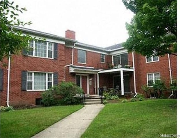 view of front of house with brick siding, a chimney, and a front lawn