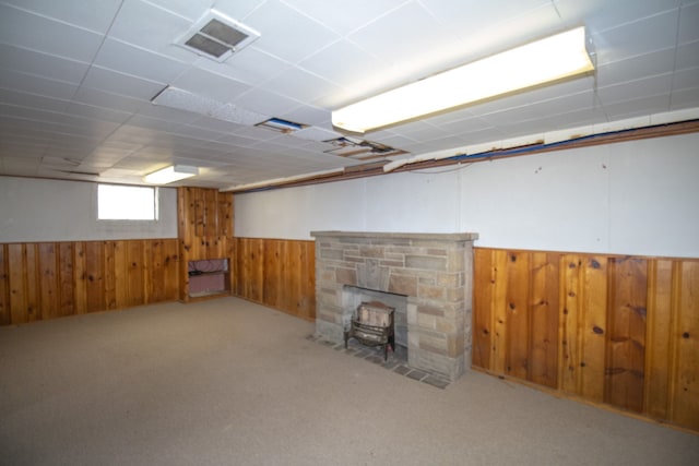 below grade area with a wood stove, carpet, visible vents, a wainscoted wall, and wooden walls