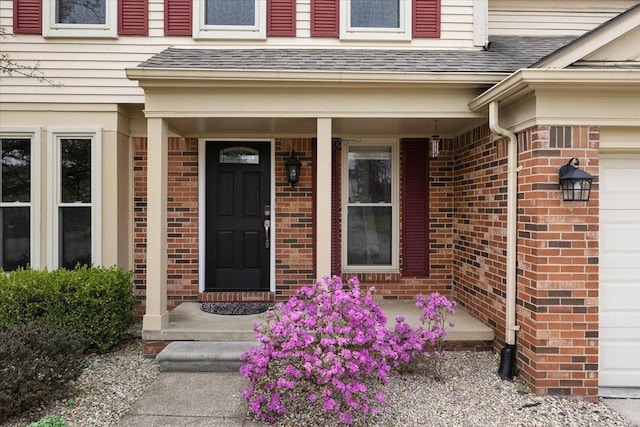 entrance to property with roof with shingles, a porch, and brick siding