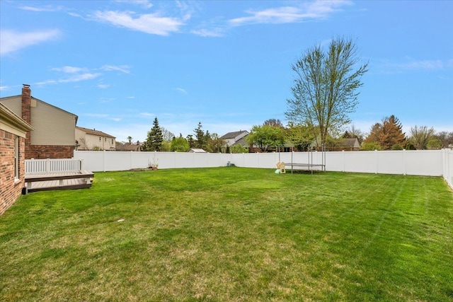 view of yard featuring a deck, a trampoline, and a fenced backyard