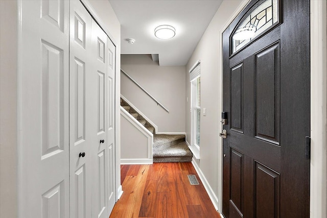 foyer with baseboards, visible vents, wood finished floors, and stairs