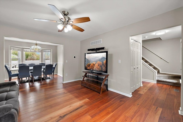 living area with a ceiling fan, hardwood / wood-style floors, stairway, and visible vents
