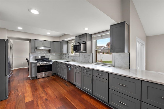 kitchen with gray cabinets, backsplash, stainless steel appliances, and under cabinet range hood