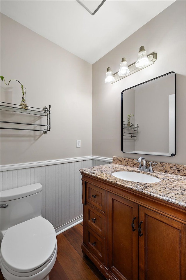 bathroom featuring toilet, wood finished floors, vanity, and wainscoting