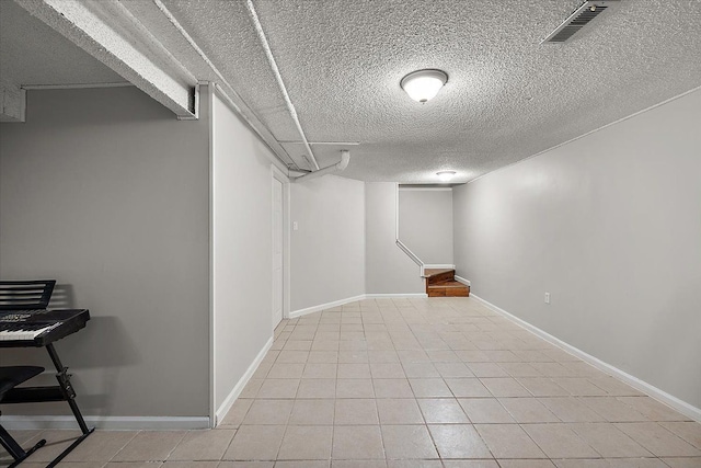 finished below grade area with baseboards, visible vents, light tile patterned floors, and a textured ceiling