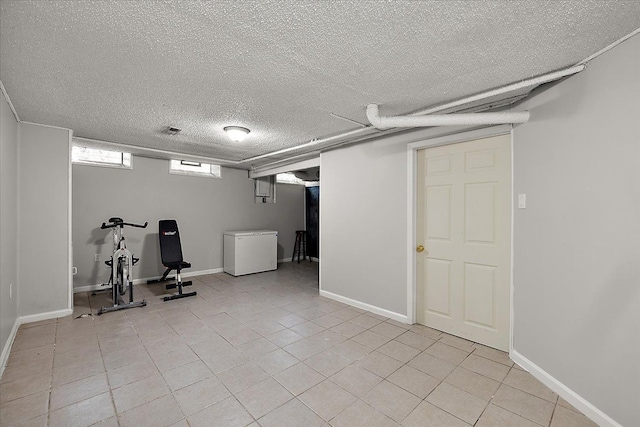 below grade area with refrigerator, light tile patterned floors, baseboards, visible vents, and a textured ceiling