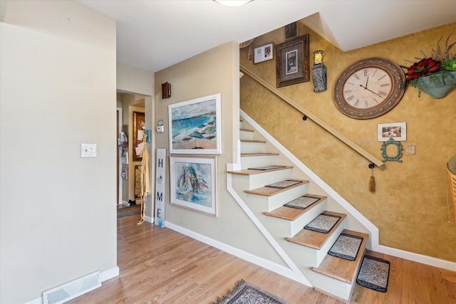 stairway with wood finished floors, baseboards, and visible vents