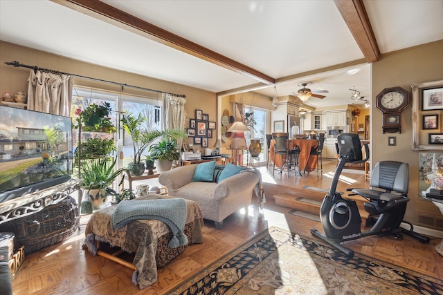 living room featuring a healthy amount of sunlight, visible vents, ceiling fan, and beam ceiling