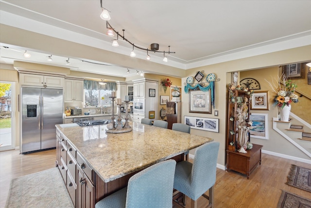 kitchen with a kitchen breakfast bar, light stone counters, stainless steel fridge, a center island, and light wood finished floors