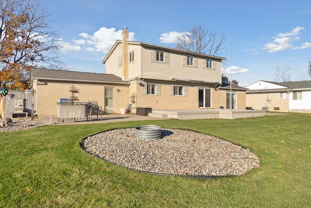 back of house with a patio, brick siding, a chimney, and a lawn