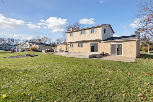 rear view of house featuring a patio area, brick siding, a lawn, and a chimney