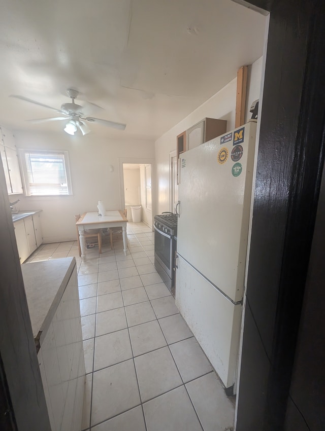 kitchen featuring a ceiling fan, freestanding refrigerator, stainless steel gas range oven, and light tile patterned floors