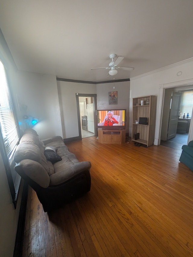 living room featuring ornamental molding, wood-type flooring, baseboards, and a ceiling fan