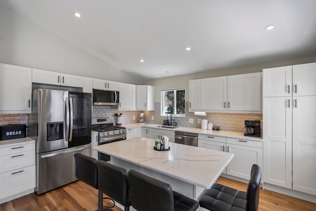 kitchen featuring white cabinets, a sink, appliances with stainless steel finishes, a breakfast bar, and vaulted ceiling