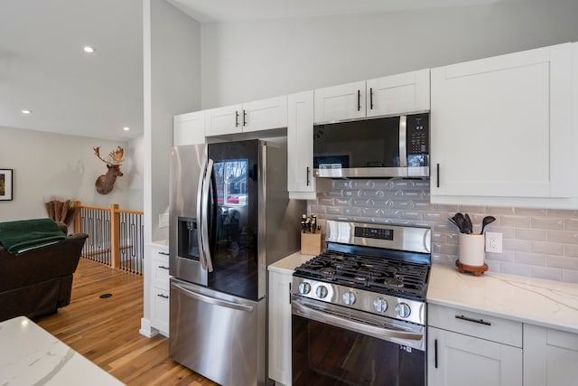 kitchen with white cabinets, appliances with stainless steel finishes, light wood finished floors, light stone countertops, and backsplash