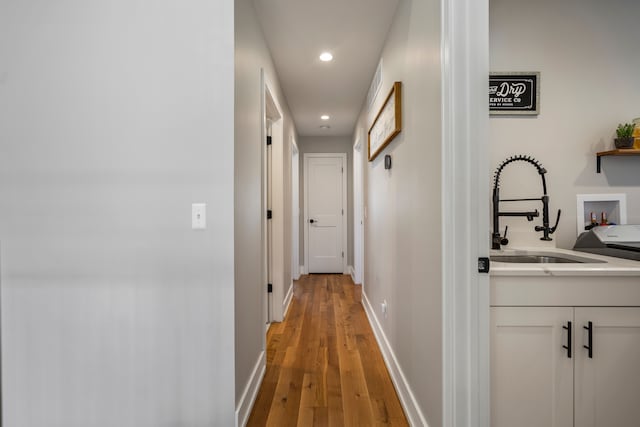 hallway with a sink, baseboards, recessed lighting, and light wood-style floors