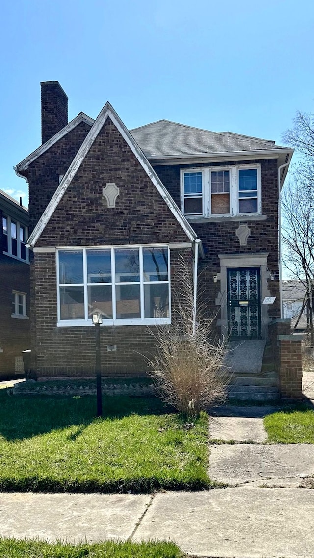 view of front facade with brick siding, a front yard, and a chimney