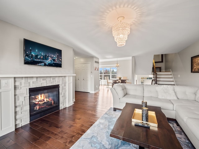 living area featuring stairway, a fireplace, wood finished floors, and a notable chandelier