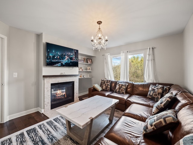 living area featuring an inviting chandelier, baseboards, dark wood-style flooring, and a premium fireplace