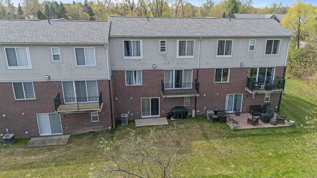 back of property with a shingled roof, brick siding, cooling unit, a patio area, and a lawn