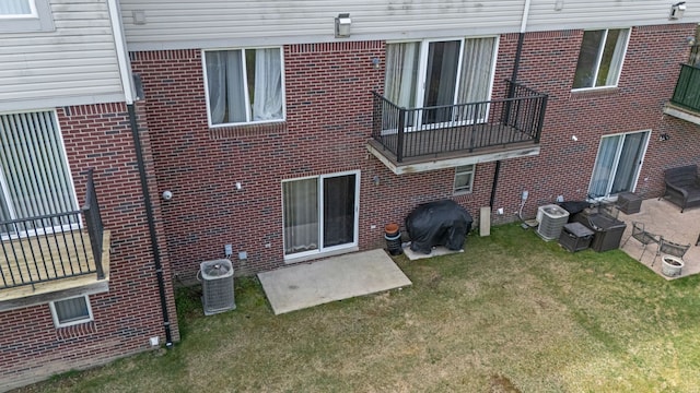 back of property with a yard, brick siding, central AC unit, and a balcony