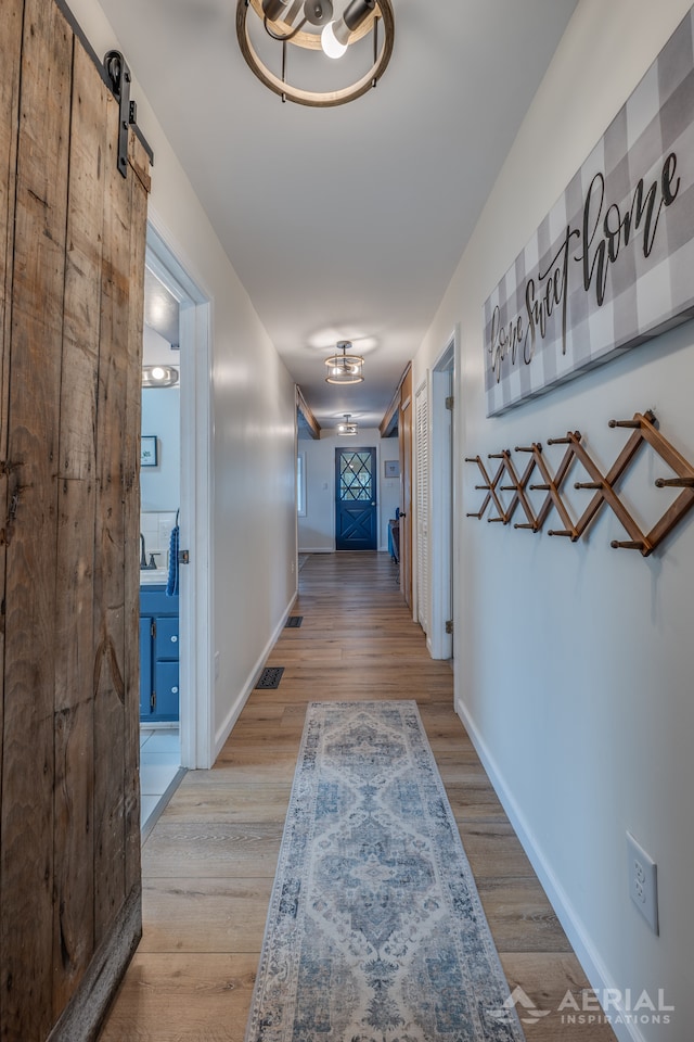 hall with a barn door, baseboards, wood finished floors, and visible vents