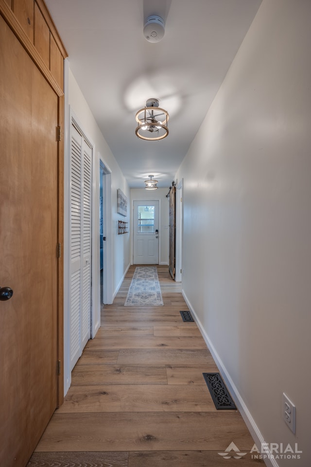 hall featuring baseboards, a notable chandelier, visible vents, and light wood-style flooring
