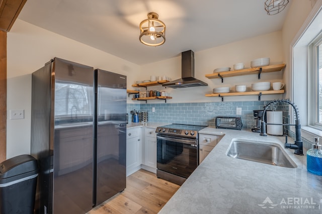 kitchen featuring stainless steel appliances, open shelves, a sink, light wood-type flooring, and wall chimney exhaust hood