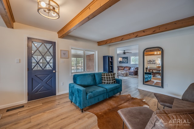 living area featuring beamed ceiling, light wood-style flooring, visible vents, and baseboards