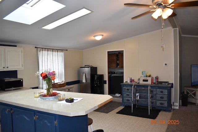 kitchen featuring vaulted ceiling with skylight, separate washer and dryer, freestanding refrigerator, carpet, and blue cabinetry