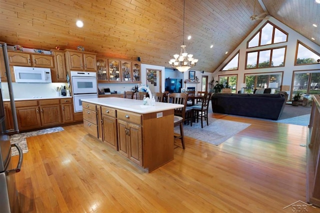 kitchen with brown cabinets, an inviting chandelier, white appliances, high vaulted ceiling, and light wood-style flooring