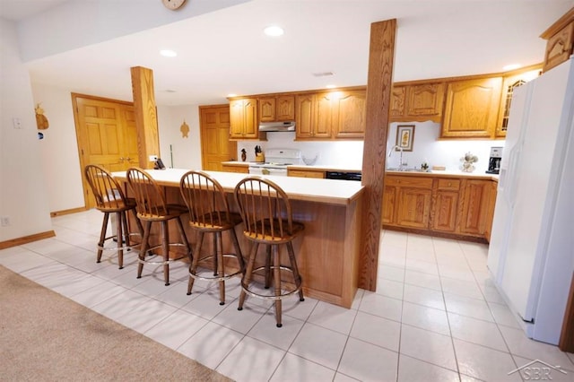 kitchen with brown cabinetry, under cabinet range hood, white appliances, and a kitchen bar