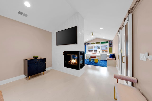 living room featuring visible vents, a barn door, a brick fireplace, a ceiling fan, and vaulted ceiling