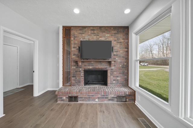 unfurnished living room featuring baseboards, wood finished floors, visible vents, and a fireplace