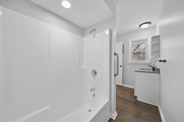bathroom featuring shower / washtub combination, wood finished floors, baseboards, and a sink