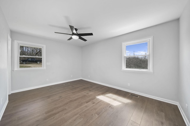 unfurnished room featuring dark wood-type flooring, visible vents, a ceiling fan, and baseboards