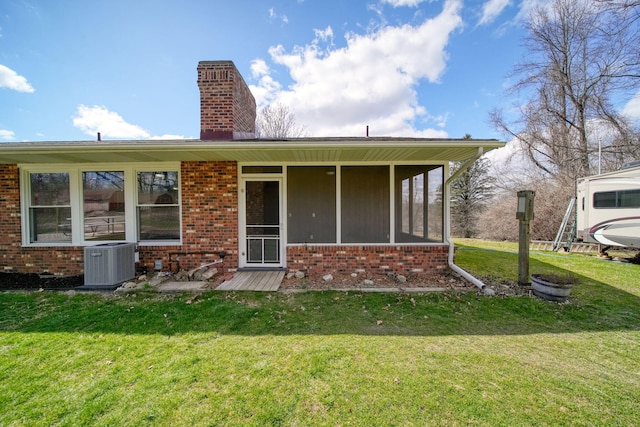 rear view of property featuring a chimney, central AC unit, brick siding, and a yard