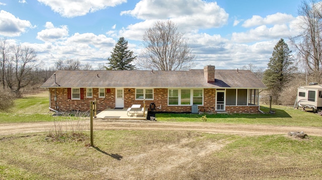 ranch-style home featuring a chimney, brick siding, cooling unit, and a front yard