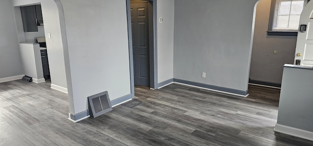 empty room with dark wood-style flooring, visible vents, and arched walkways