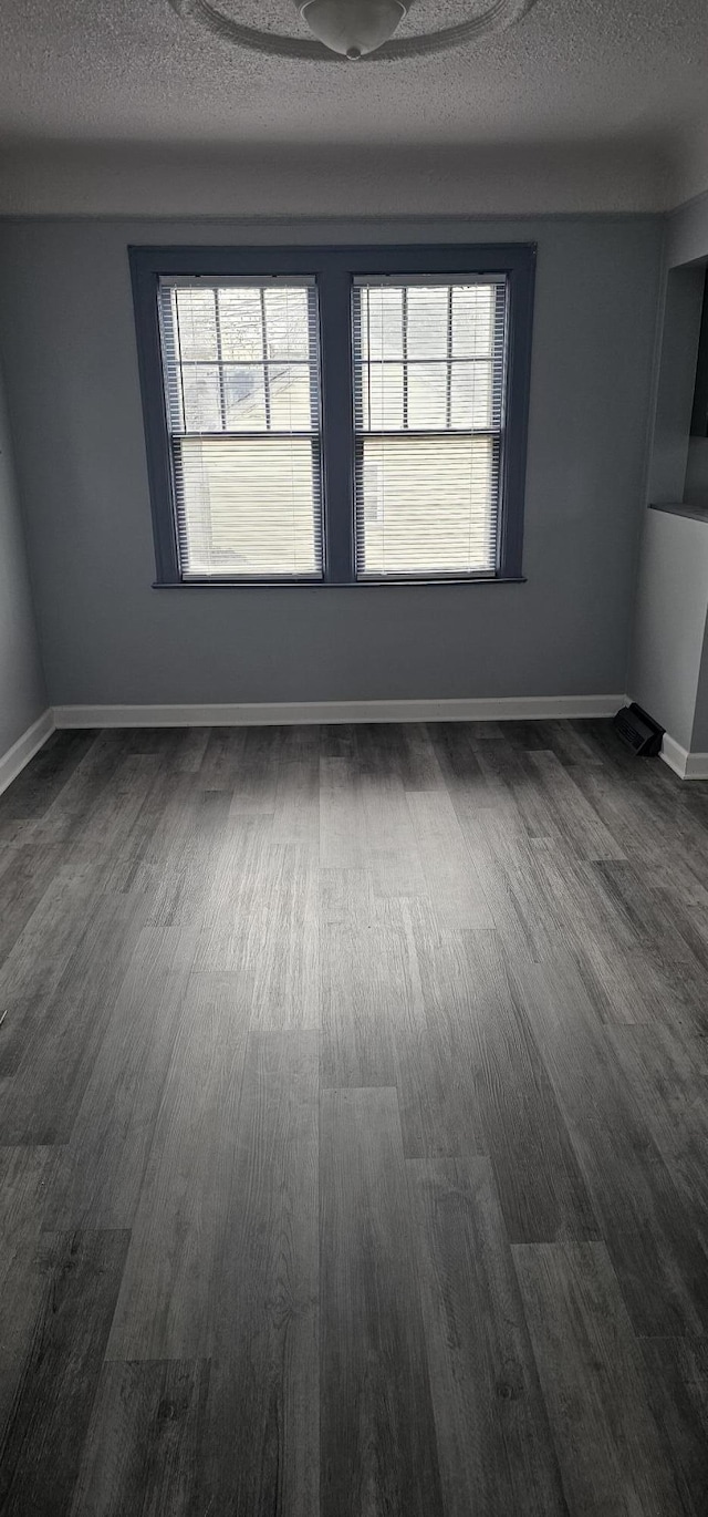 unfurnished room featuring baseboards, a textured ceiling, and dark wood finished floors