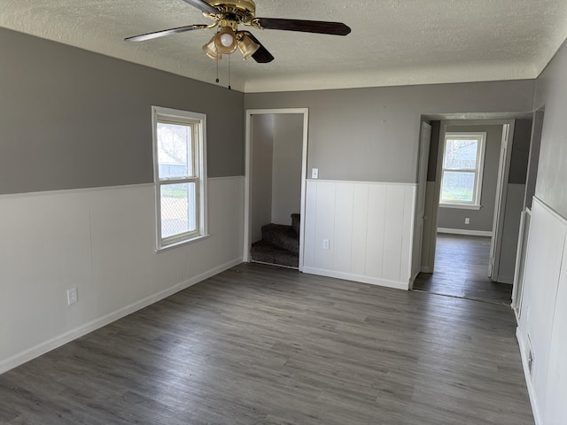 empty room featuring dark wood finished floors, ceiling fan, wainscoting, and stairs