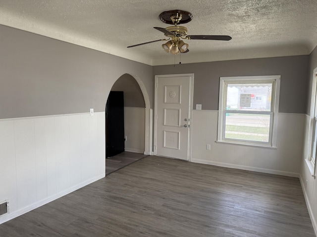 empty room with ceiling fan, arched walkways, wood finished floors, and a textured ceiling